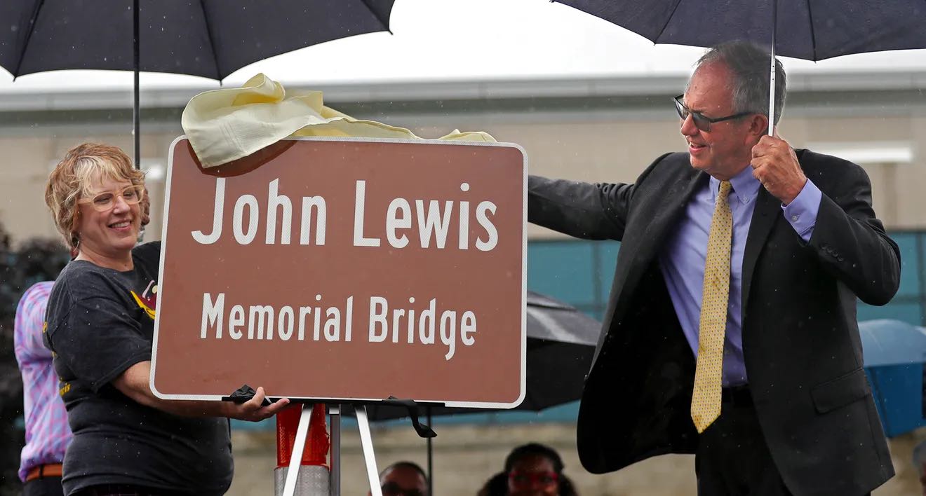 Mayor John Pribonic pulls away a sheet to reveal a sign dedicating the Steels Corners bridge, as the John Lewis Memorial Bridge, on Saturday, in Stow — courtesy of Jeff Lange, Akron Beacon Journal.