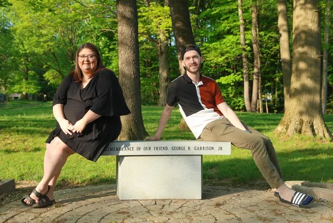 Melissa Anderson and Aaron Yeager sit at the memorial they helped bring to fruition, to honor the memory of their late friend, George R. Garrison, Jr. The memorial will also acknowledge those who have felt marginalized, and let all Stow residents and visitors know that they are welcome, seen, and respected here — courtesy of Nicholas McLaughlin, Akron Beacon Journal.